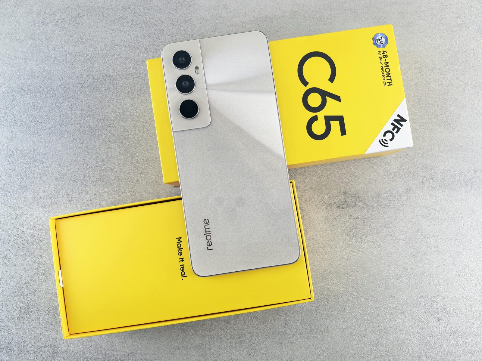 A sleek smartphone placed on a vibrant yellow box against a gray background, showcasing modern technology.